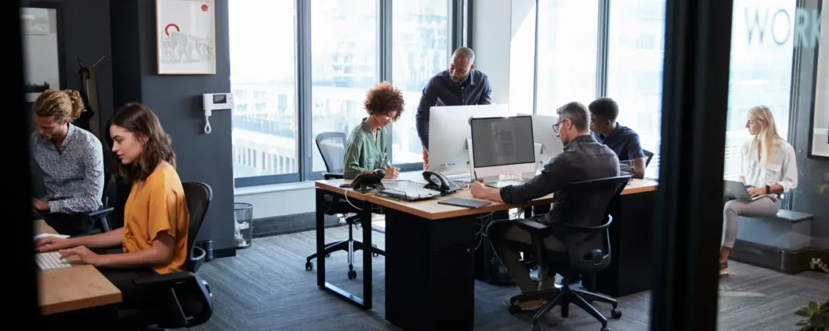 Um escritório com pessoas em volta da mesa utilizando computadores